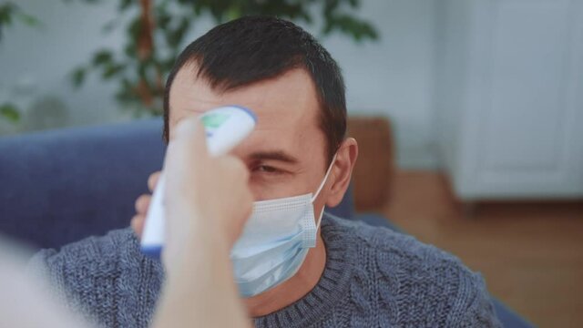 a man in a medical mask has his temperature measured with a digital thermometer. coronavirus lockdown stay home social covid 19 distance. temperature measurement mode during coronavirus