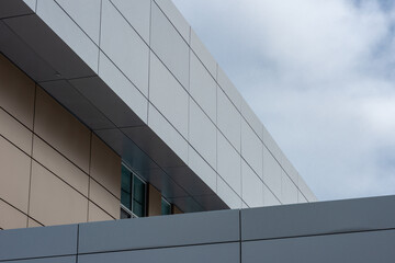 Obraz premium The exterior wall of a contemporary commercial style building with aluminum metal composite panels and glass windows. The futuristic building has engineered diagonal cladding steel frame panels. 