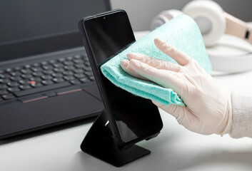 Woman in gloves wipes phomewith wet tissue and disinfectant during covid 19. Protection hygiene prevention from infection, germs, bacteria. Disinfection phomeand laptop keyboard alcohol disinfectant