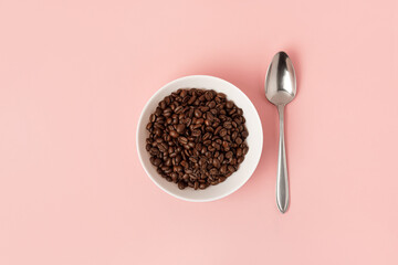 Coffee beans in white cup and spoon on pink background. Flat lay.