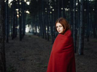 A woman with a red plaid on her shoulders among the trees in the forest