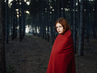 Naklejka premium A woman with a red plaid on her shoulders among the trees in the forest