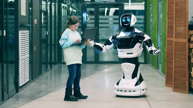 Little girl operating a robot with a laptop. Futuristic technology concept.