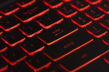 Black gaming keyboard with red backlight. Closeup focused on ENTER key.