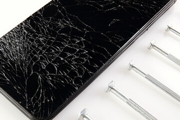 A broken smartphone screen with cracks lies next to the screwdrivers. Background for a gadget and electronics repair shop. Close-up.