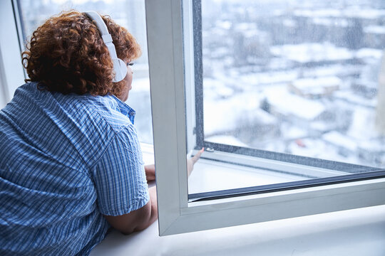 Rear-view photo of charming lady enjoying music and window view