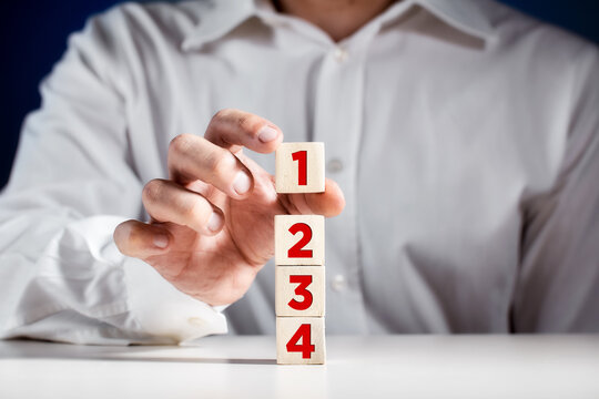 Businessman hand puts a wooden block with the number one on top of the tiered cubes. First step, level or rank - Powered by Adobe