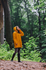 woman in yellow raincoat walking by rainy forest