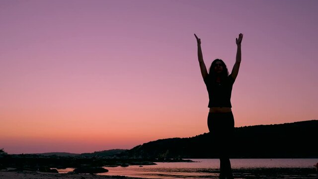 Silhouette of woman doing relaxation and breathing exercises rising arms on the beach during sunset or sunrise light. Breth of fresh air concept