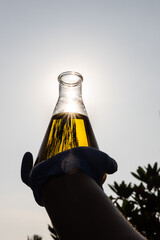 Silhouette of hand with gloves holding beaker with ethanol biofuel against blue sky