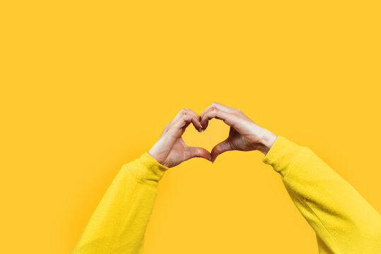 Hands making heart shape isolated on a yellow background - Love and minimal fashion concept