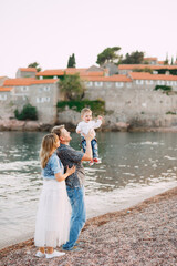 Fototapeta na wymiar Mom and dad are holding their little son in their arms by the sea against the backdrop of the Sveti Stefan island
