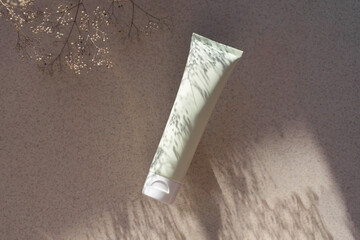light green cosmetic tube for face, hand or body cream with plant shadow on sunlit background.