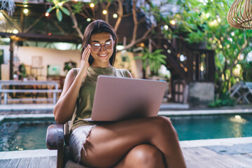 Joyful ethnic woman browsing laptop on poolside