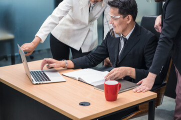 Asian female manager consulting and collaborating with colleagues working with laptop at desk in the office