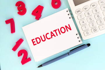 The word education is written in red letters on a white notebook that lies next to red numbers and a white calculator. Educational concept