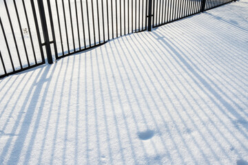 The shadow from a metal fence falls on clean snow, on a winter sunny day. 