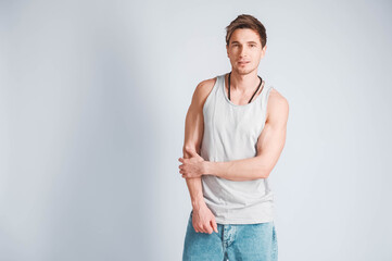 Young muscular man in a light T-shirt and jeans on a white background. Copy, empty space for text