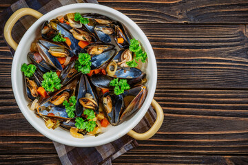 Boiled mussels in cooking dish with parsley on a wooden background
