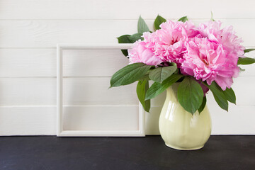 Pink peonies with whith  photo frame on a white  wooden board, empty  space for text. Floral mock up