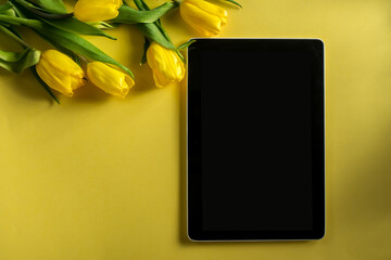 Mockup computer tablet with bouquet of tulips on top view on colorful yellow background, panoramic shot