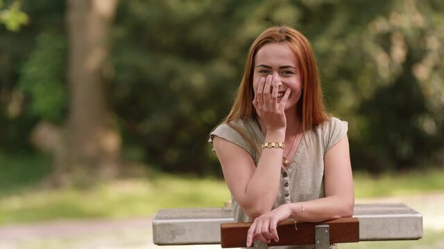 [4k] cute young redhead giggling at table in public park
