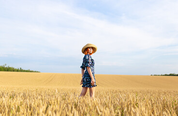 A girl stands in a golden field of wheat. A young girl in a romantic hat among the ears of wheat at sunset.