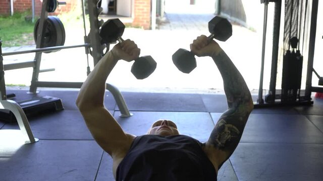 Tattoo man muscles in home gym doing dumbbell inward tricep press shot from front