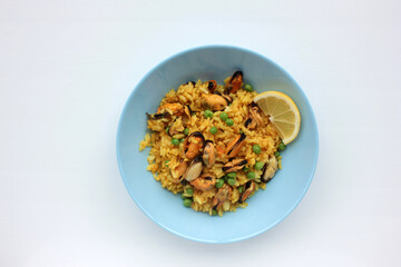Traditional Spanish seafood dish paella with lemon slice on table. Mussel risotto with green peas on blue plate on white background. Top view, copy space. Healthy eating concept
