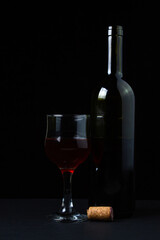 A glass of homemade wine next to a bottle on a dark background. Glass of red wine on a black background. Alcoholic drink
