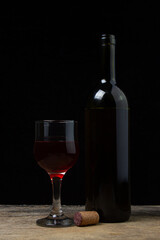 A glass of homemade wine next to a bottle on a dark background. Glass of red wine on a black background. Alcoholic drink