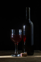 A glass of homemade wine next to a bottle on a dark background. Glass of red wine on a black background. Alcoholic drink