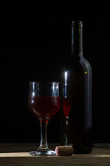 A glass of homemade wine next to a bottle on a dark background. Glass of red wine on a black background. Alcoholic drink