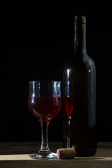 A glass of homemade wine next to a bottle on a dark background. Glass of red wine on a black background. Alcoholic drink