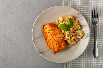 Baked chicken breast on a gray plate with pineapple salad on a table on a napkin on a concrete background near a fork.