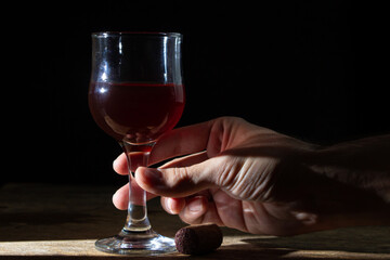 The hand takes a glass of red homemade wine. Glass of red wine on a black background. Alcoholic beverage
