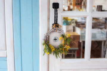 Front Door with wreath of Mimosa yellow flowers. Easter wreath. Spring decoration on wooden door of house. Home entrance with decorative Spring wreath on door. Rustic interior element of spring porch	