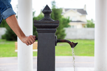 Man hand opening tap on drinking column, jet of water. Сity water tap with drinkable water in...