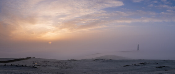 The sun rising above a lighthouse in the mist