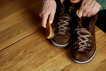 Man's hand clean suede shoes, boots with a brush on wooden background.