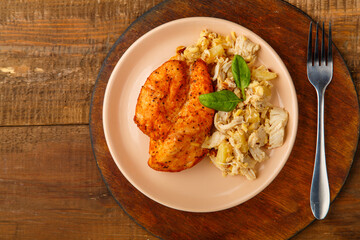 Baked chicken breast on a beige plate with pineapple salad on a table on a round stand next to a fork.