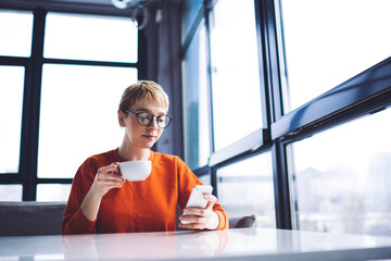 Serious woman chatting on smartphone and drinking coffee