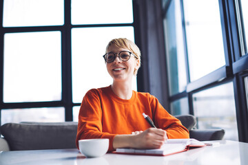 Cheerful woman making notes while working in cafe