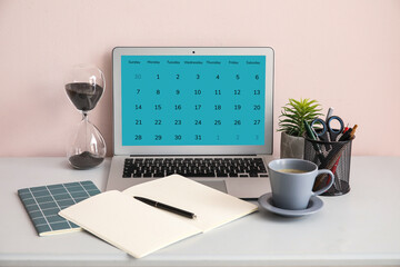 Laptop with open calendar application, stationery and cup of coffee on table