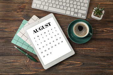 Tablet computer with open calendar application, stationery and cup of coffee on table