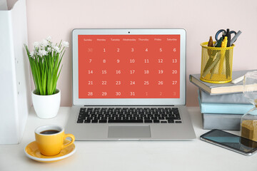 Laptop with open calendar application, stationery and cup of coffee on table