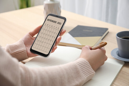 Woman with mobile phone using calendar application at table
