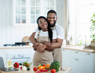 Portrait Of Romantic Black Spouses Embracing In Kitchen While Cooking Lunch Together