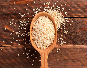 Sesame seeds in a spoon and scattered on a wooden background. Top view