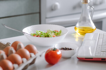 Online cooking. Preparing salad using digital cookbook. Fresh vegetables and laptop